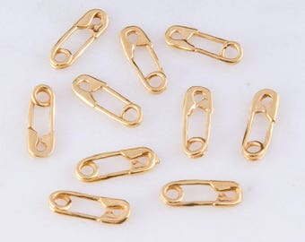 Könnte beinhalten: Zehn goldfarbene Sicherheitsnadeln, jede mit einem einfachen Design. Diese Nadeln sind klein und zart, perfekt, um Schmuck oder Bastelarbeiten mit einem Hauch von Verspieltheit zu versehen.