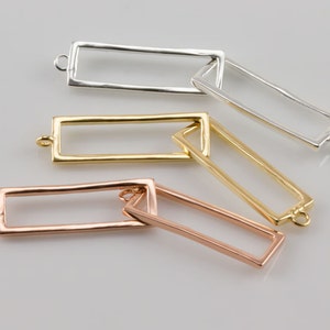 Könnte beinhalten: Drei rechteckige Metallrahmen in Silber, Gold und Roségold. Jeder Rahmen hat oben und unten eine kleine Schlaufe.