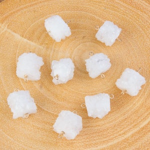 May include: Eight white crystal gemstone beads with gold jump rings. The beads are irregular in shape and have a rough, natural texture.