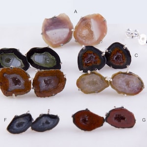 May include: Set of seven pairs of agate earrings. Each pair features a unique geode slice with different colors and patterns, including brown, black, white, and green. The earrings are set in silver.
