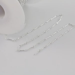 May include: A silver chain with small, round links. The chain is laid out on a white surface.