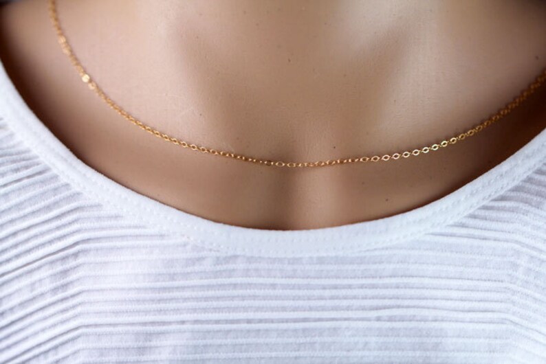 Pu&ograve; includere: Una delicata collana a catena d'oro su un manichino bianco.
