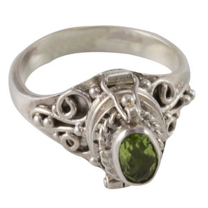 May include: A silver ring with an ornate design and a green gemstone. The ring has a hinged compartment that can be opened to reveal a small space for holding a small item.