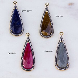 May include: Four teardrop-shaped gemstone pendants with gold settings and a border of clear stones. The stones are dyed sapphire, tiger eye, dyed ruby, and labradorite.