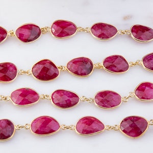 Könnte beinhalten: Eine Kette aus rubinroten Edelsteinperlen, die durch goldene Kettenglieder verbunden sind. Die Perlen sind oval geformt und haben eine facettierte Oberfläche.
