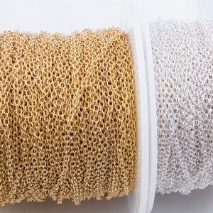 May include: Two spools of chain, one gold and one silver, are wound around white spools. The chain is a delicate, linked design.