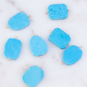 May include: Seven turquoise gemstone pendants with gold jump rings. The turquoise stones are all different shapes and sizes, but they are all a light blue color.