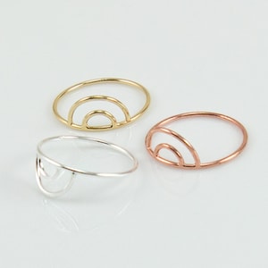 May include: Three simple minimalist rings with an arch design. The rings are made of silver, gold, and rose gold.