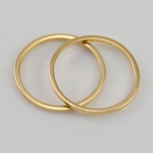 May include: Two gold-colored metal rings interlocked together. The rings are smooth and round.