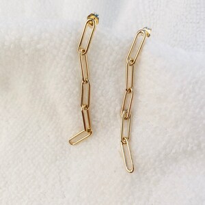 May include: A pair of gold chain earrings with a simple, modern design. Each earring features a series of connected oval-shaped links.