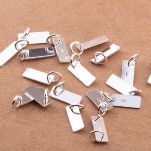 May include: A collection of silver-toned metal rectangular tags with jump rings. The tags are blank and ready for personalization.