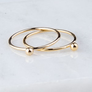 May include: Two gold rings with a small ball at the end of each ring.