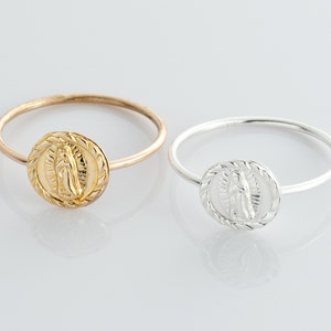 Könnte beinhalten: Zwei schlichte Silberringe mit einem erhabenen Bild der Jungfrau Maria auf der Vorderseite. Der Ring links ist golden, der Ring rechts ist silber.