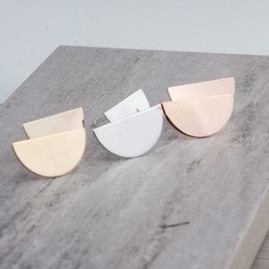 Puede incluir: Tres pares de pendientes con un diseño de medio círculo. Los pendientes están hechos de metal y vienen en oro, plata y oro rosa.