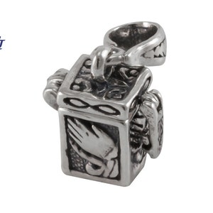 May include: A silver charm in the shape of a small box with an intricate design. The box has a hinged lid and a small loop for attaching to a chain. The box is decorated with a praying hands design and an infinity symbol.