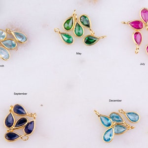 May include: Gold-toned teardrop-shaped pendants with various colored gemstones, including light blue, green, and pink. The image includes text labels: "March", "May", "July", "September", and "December".