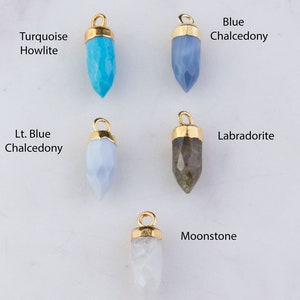 May include: Five different gemstone pendants with gold settings. The stones are turquoise howlite, blue chalcedony, light blue chalcedony, labradorite, and moonstone.