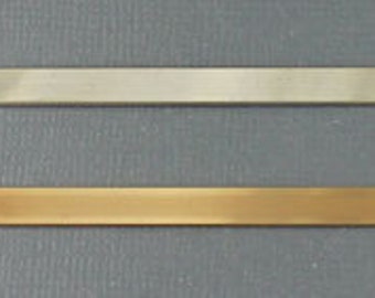May include: Two metal bars, one silver and one gold, are lying flat on a gray surface. The bars are both rectangular and have rounded edges.