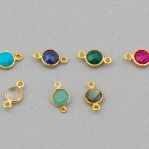 May include: Seven gold-toned connector charms with different colored gemstones. The gemstones are turquoise, blue, green, red, clear, green, and gray.