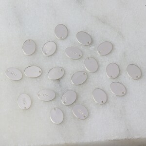 May include: A collection of 18 silver oval-shaped metal charms with a hole at the top. The charms are blank and ready to be personalized.