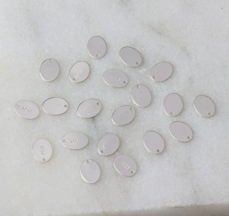 May include: A collection of 18 silver oval-shaped metal charms with a hole at the top. The charms are blank and ready to be personalized.