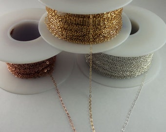 May include: Three spools of chain, one gold, one silver, and one rose gold. The chains are on white spools and are hanging down.