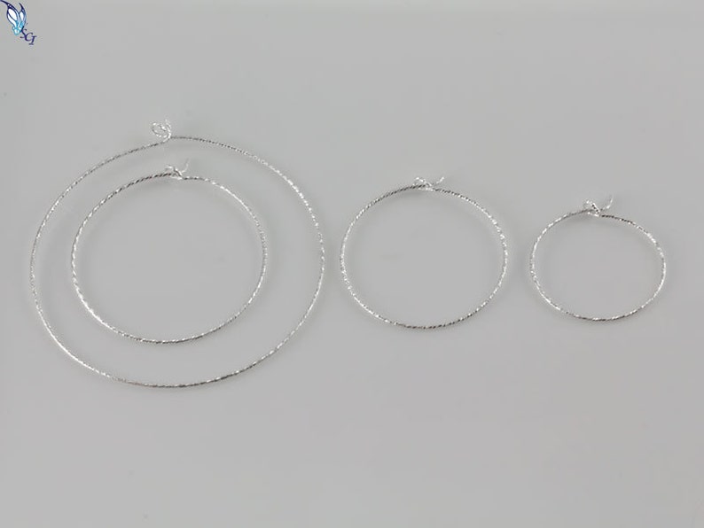 May include: Three silver hoop earrings of different sizes. The hoops are all textured and have a shiny finish.