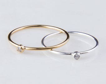 May include: Two simple rings, each with a single clear stone. One ring is gold and the other is silver.