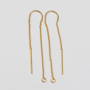 May include: A pair of gold-toned earrings with a dangling chain and a straight bar. The earrings have a small loop at the top and a larger loop at the bottom.