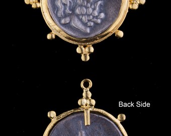 May include: A gold pendant with a silver coin featuring a profile of a person's head on one side and a standing figure on the other side. The pendant is attached to a gold chain with a decorative design.