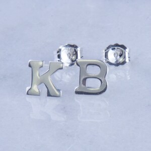 May include: A pair of silver initial earrings, one with the letter K and the other with the letter B.