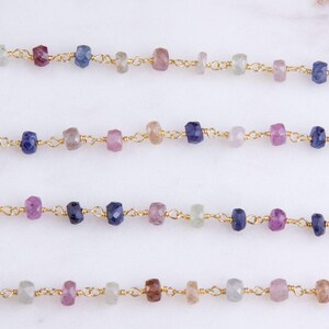 May include: A strand of gold chain with faceted gemstone beads in shades of blue, pink, and green. The beads are evenly spaced and connected by small gold links.
