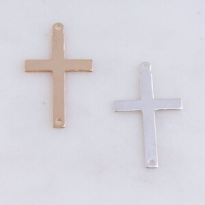 May include: Two metal cross charms, one gold and one silver. Both charms have a simple, classic design.