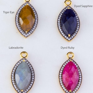 May include: Four gemstone pendants with a gold setting and a clear crystal halo. The gemstones are tiger eye, dyed sapphire, labradorite, and dyed ruby.