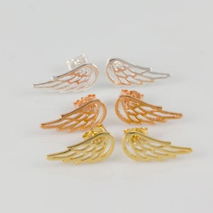 May include: Three pairs of wing-shaped stud earrings in silver, rose gold, and gold. The earrings are displayed on a white surface. Each wing has a detailed, openwork design.