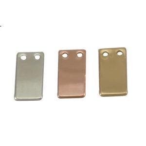 May include: Three rectangular metal tags with two holes each. The tags are silver, rose gold, and gold.