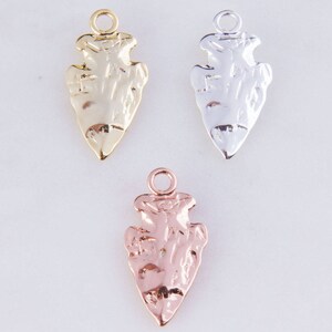 Könnte beinhalten: Drei Pfeilspitzen-Anhänger in Gold, Silber und Roségold. Jeder Anhänger hat ein detailliertes Pfeilspitzen-Design mit einer Öse oben zum Anbringen an Schmuck.