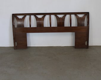 May include: A dark brown wooden headboard with a unique, geometric design. The headboard has a curved top and a rectangular base.