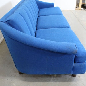 May include: A blue fabric sofa with a tufted back and wooden legs. The sofa has a curved armrest and is in good condition.