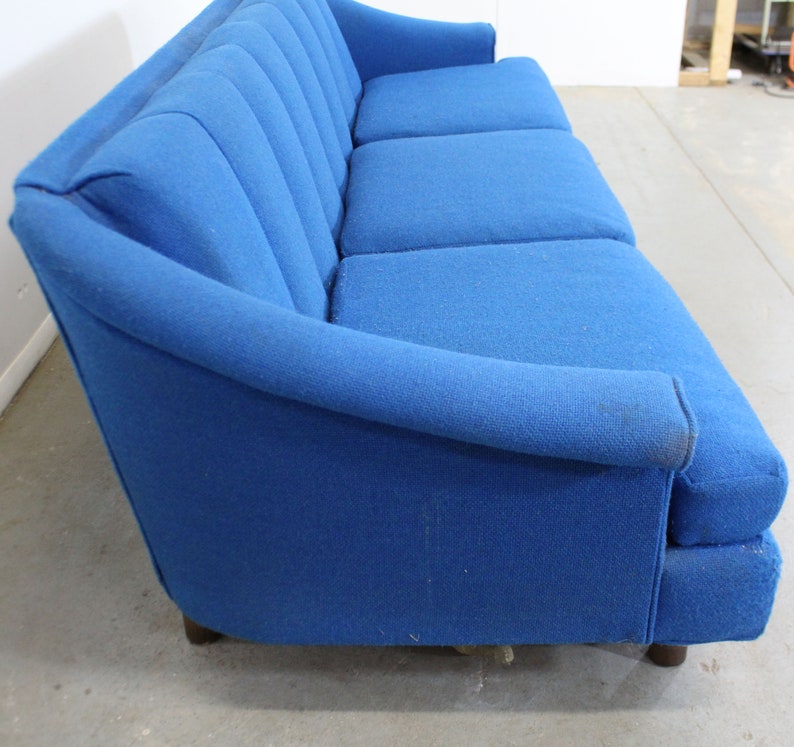 May include: A blue fabric sofa with a tufted back and wooden legs. The sofa has a curved armrest and is in good condition.