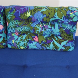 May include: A blue sofa with two floral patterned pillows. The pillows have a blue, green, and pink floral design.