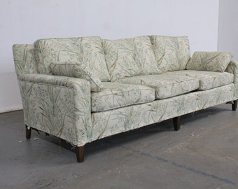 May include: A light green patterned sofa with three cushions and wooden legs. The sofa is in a light-colored room with a concrete floor.