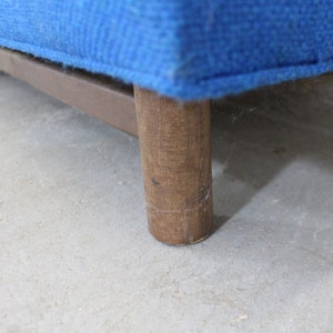 May include: Close-up of a wooden leg on a blue upholstered sofa. The leg is made of dark wood and has a rectangular shape.