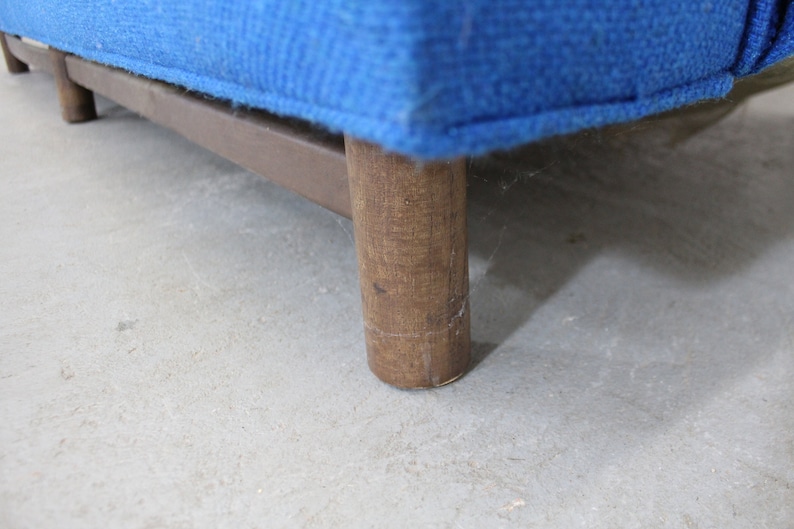 May include: Close-up of a wooden leg on a blue upholstered sofa. The leg is made of dark wood and has a rectangular shape.