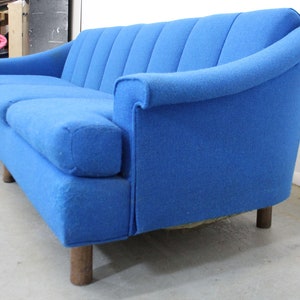 May include: A blue fabric sofa with a curved back and wooden legs. The sofa has a tufted design and is in good condition.
