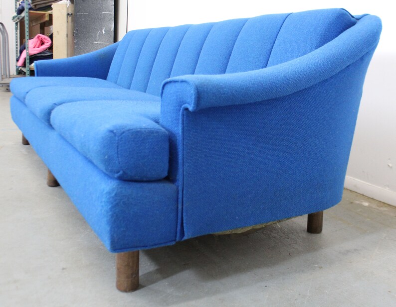 May include: A blue fabric sofa with a curved back and wooden legs. The sofa has a tufted design and is in good condition.
