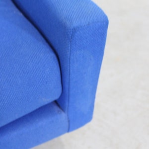 May include: Close-up of a blue fabric sofa armrest. The fabric has a subtle texture.