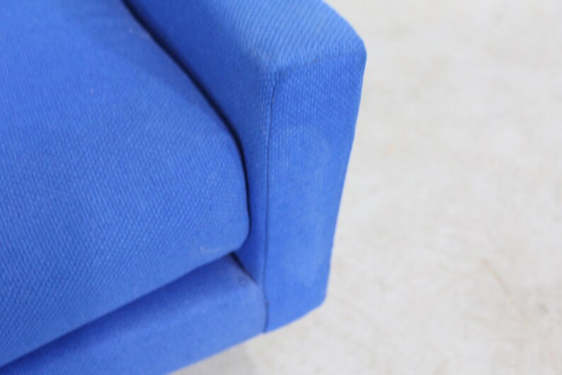 May include: Close-up of a blue fabric sofa armrest. The fabric has a subtle texture.