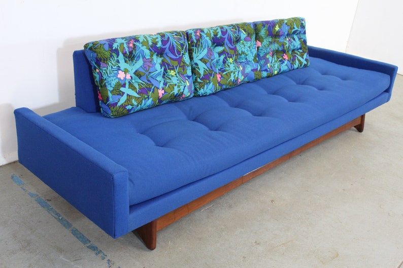 May include: A blue tufted sofa with a wooden base and three floral patterned pillows.