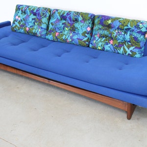 May include: A blue tufted sofa with a wooden frame and three floral patterned throw pillows.